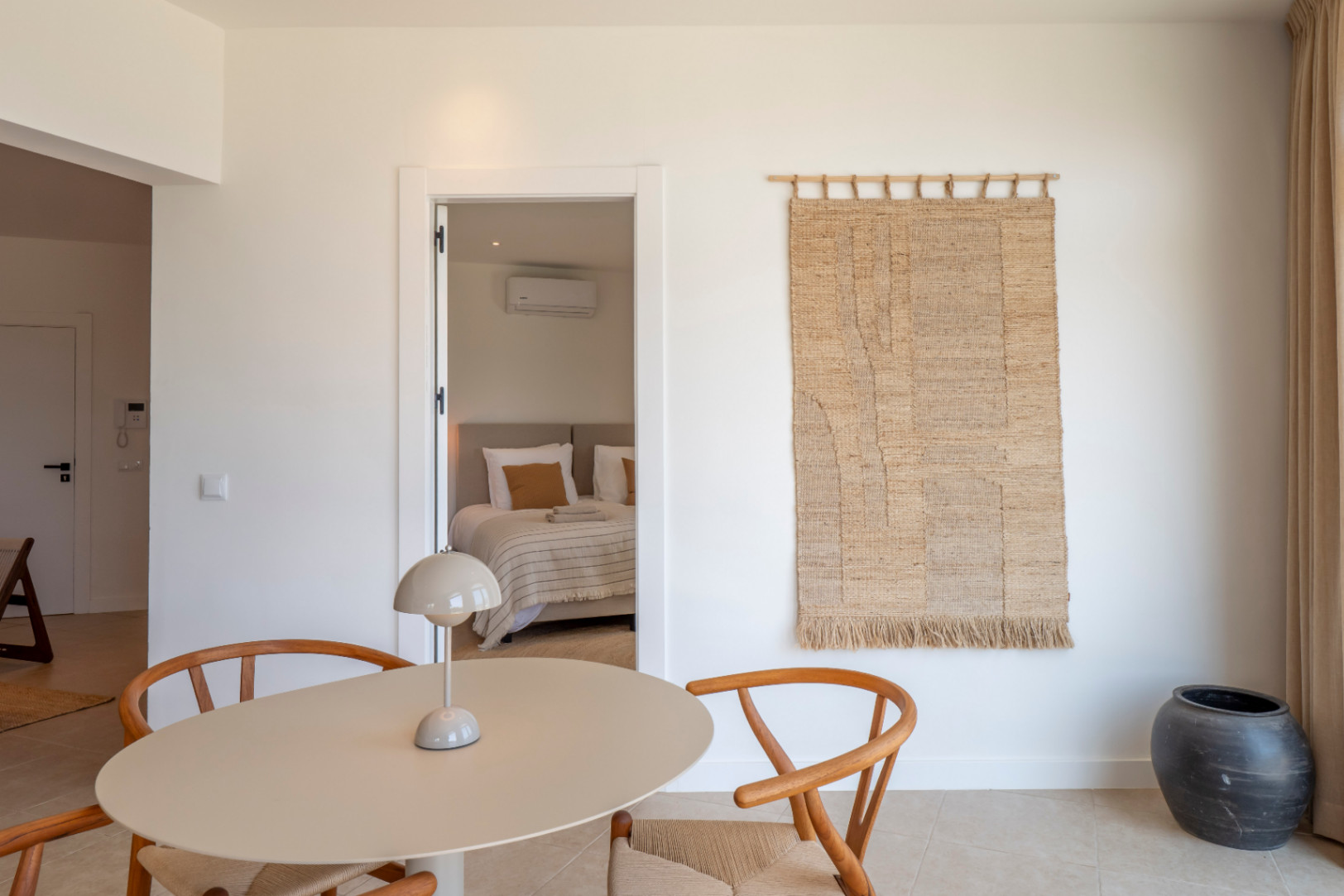 Détail intérieur avec table ronde, chaises en bois et aperçu de la chambre.