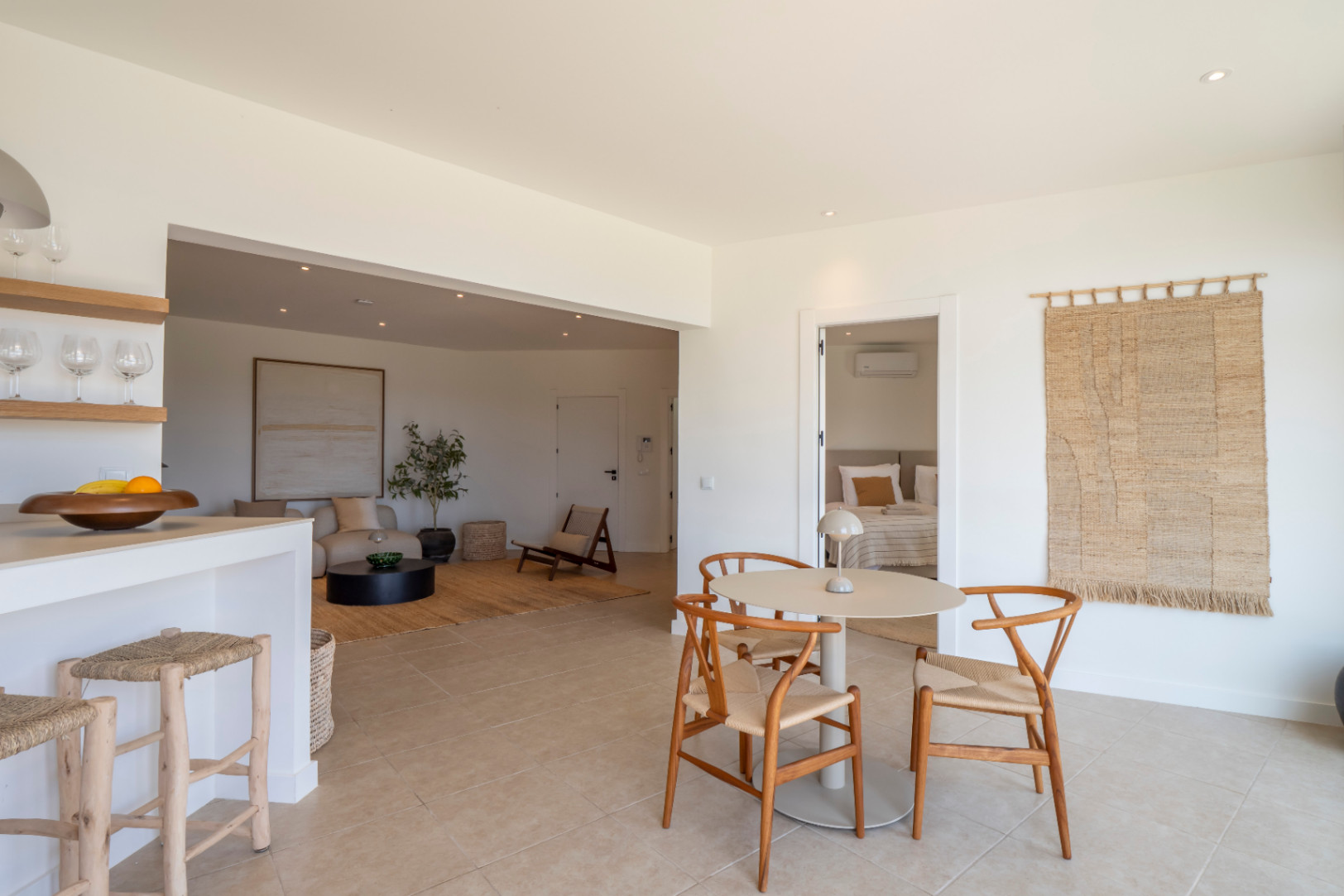Intérieurs lumineux avec table à manger ronde et chaises en bois clair, intégrés dans un espace ouvert avec salon et cuisine.