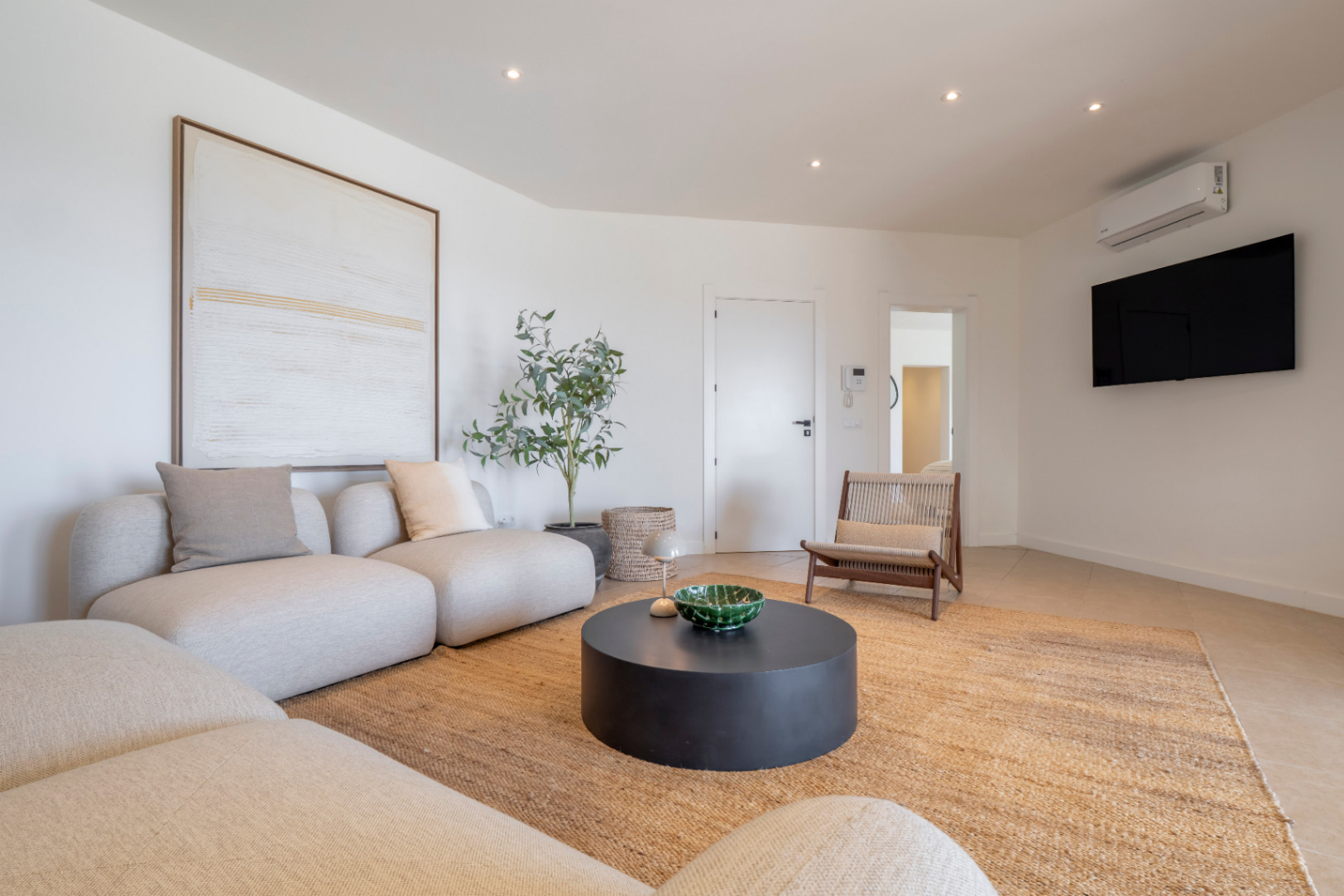 Salon lumineux avec canapé modulable, tapis en jute et table basse circulaire noire. Décor minimaliste et lumière naturelle.