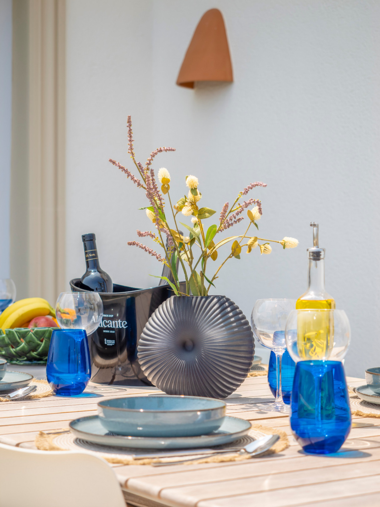 Table à manger extérieure avec vaisselle bleue, vase gris et refroidisseur à vin Alicante.