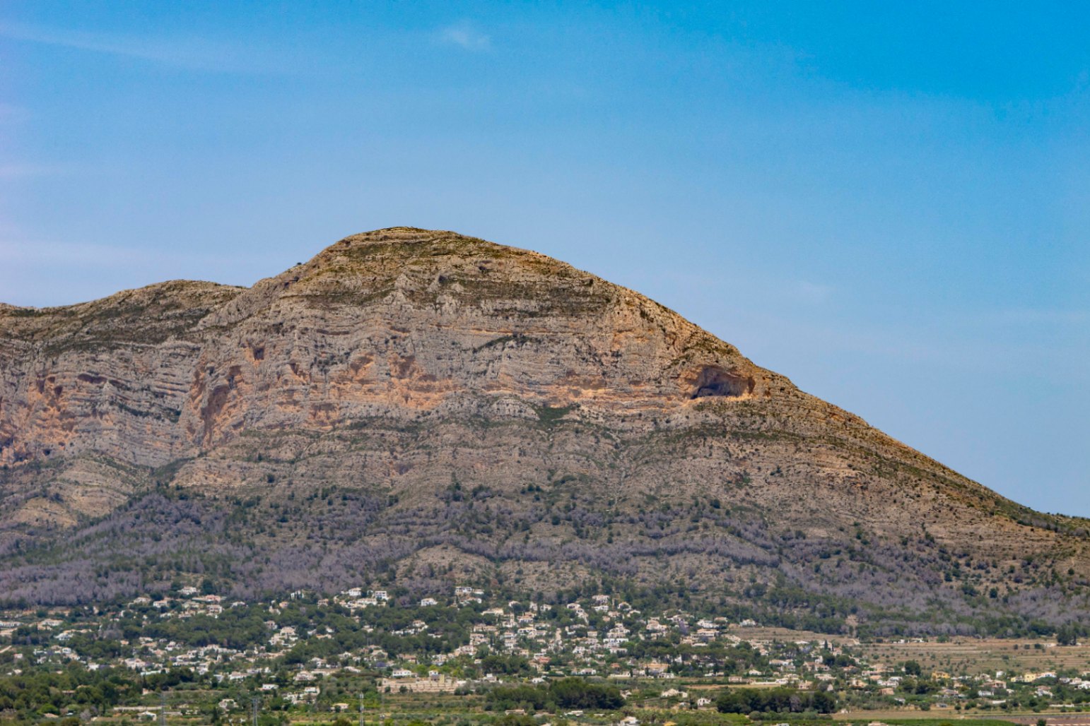 Vue panoramique sur la montagne Montgó, avec une grotte visible et des maisons dispersées à sa base.