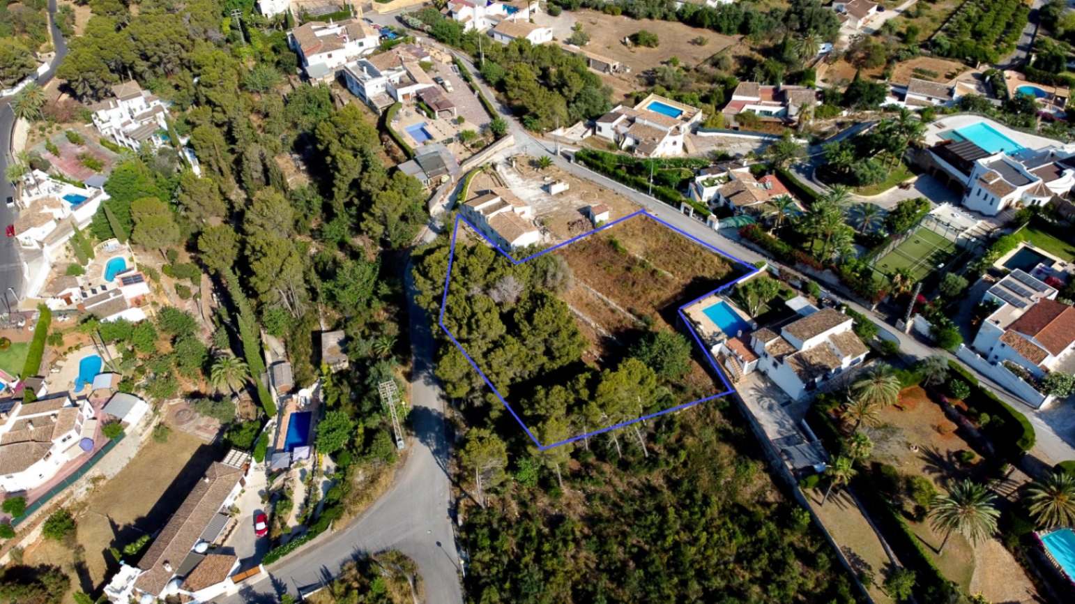 Vue aérienne du terrain urbain de 1 908 m² délimité en bleu, montrant sa zone boisée de pins et son intégration dans un quartier résidentiel calme de Jávea.