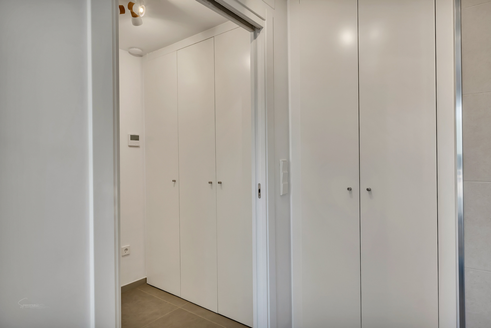 Armoires encastrées du sol au plafond avec une finition blanche minimaliste, situées dans un couloir moderne doté d'un panneau de commande numérique et d'un sol en grès.