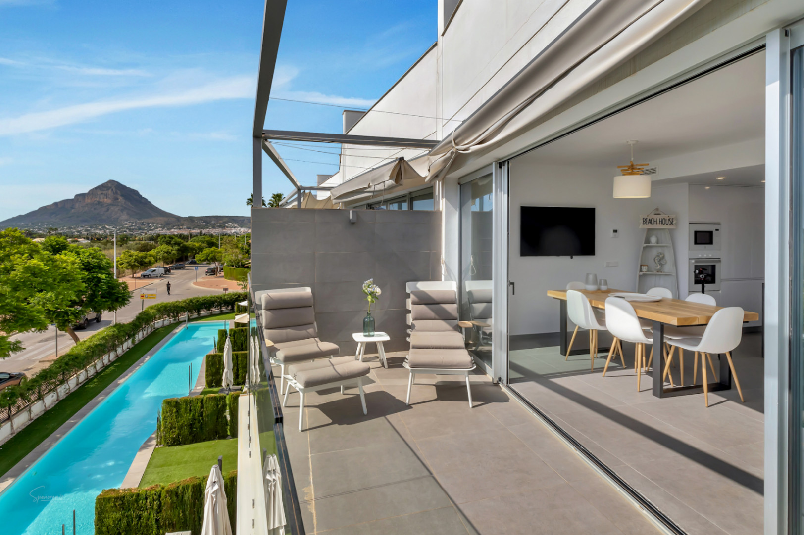 Balcon avec mobilier de détente offrant une vue sur la piscine et les montagnes. Les baies vitrées coulissantes relient l'extérieur à la salle à manger.
