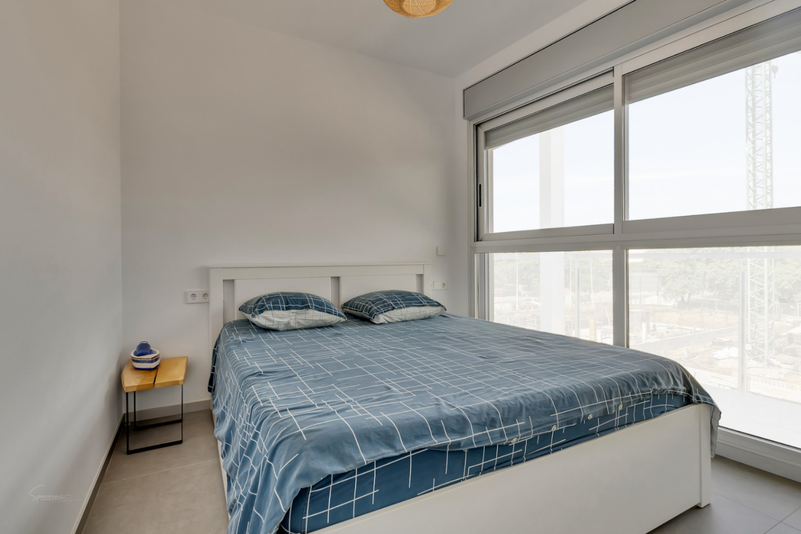 Chambre lumineuse avec lit double, grande baie vitrée en aluminium gris dotée de volets motorisés et sol en carrelage contemporain.