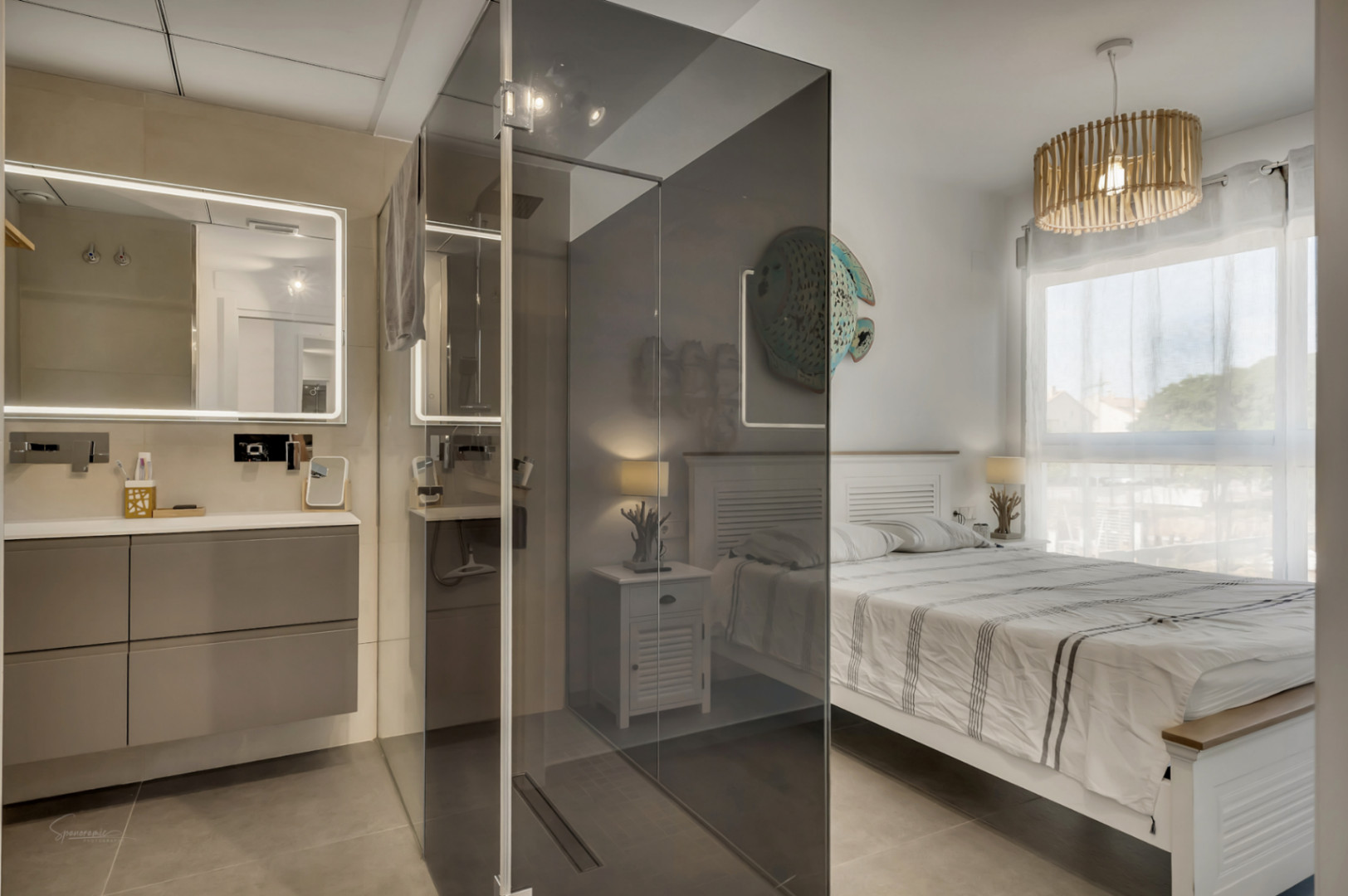 Chambre principale avec salle de bain intégrée, comprenant une douche à l'italienne avec paroi en verre fumé et un meuble vasque suspendu rétroéclairé.