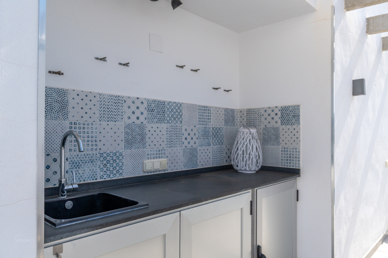 Cuisine d'été extérieure avec plan de travail sombre, évier intégré et crédence en carreaux de faïence aux motifs bleus et blancs.