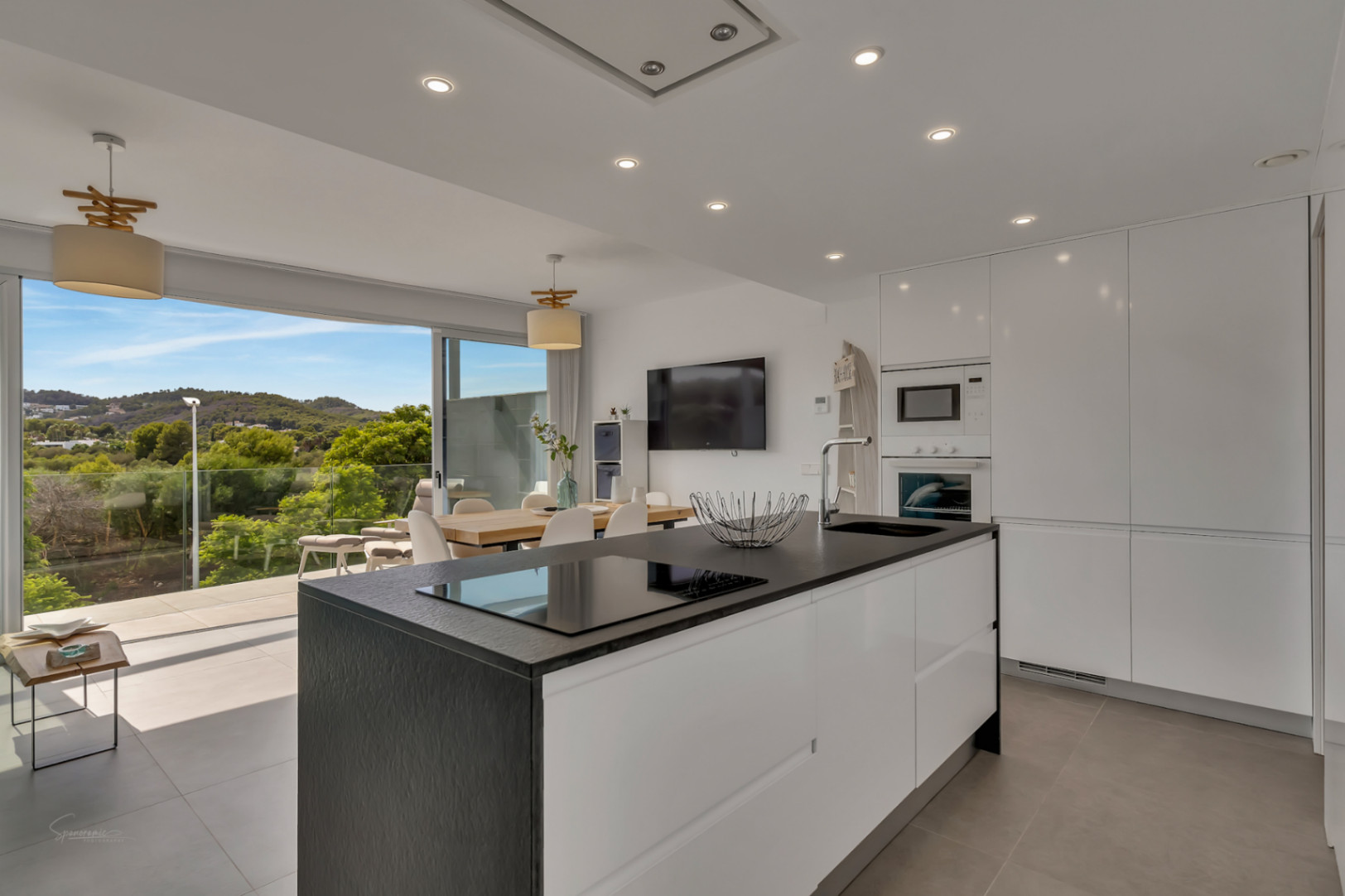 Cuisine moderne à aire ouverte avec îlot central noir, électroménagers intégrés et accès direct à une terrasse offrant une vue sur la nature environnante.