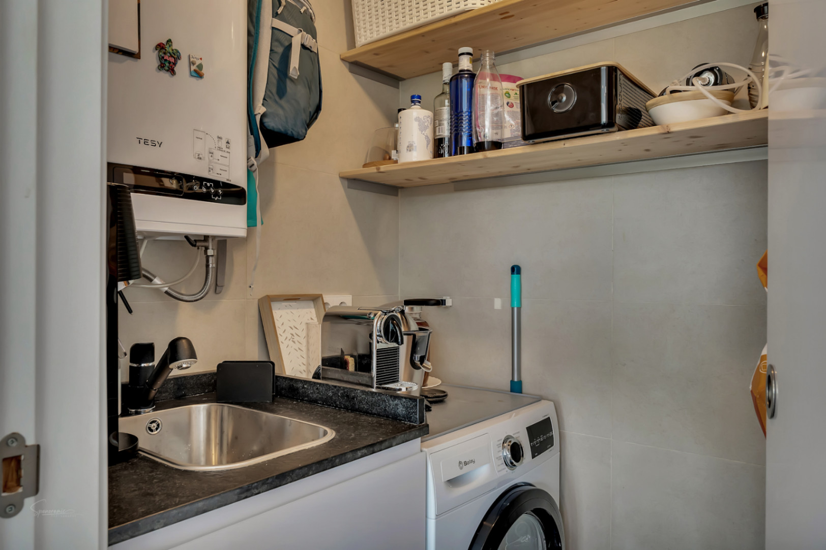 Espace buanderie fonctionnel équipé d'un lave-linge Balay, d'un évier en inox, d'un chauffe-eau électrique Tesy et d'étagères en bois.