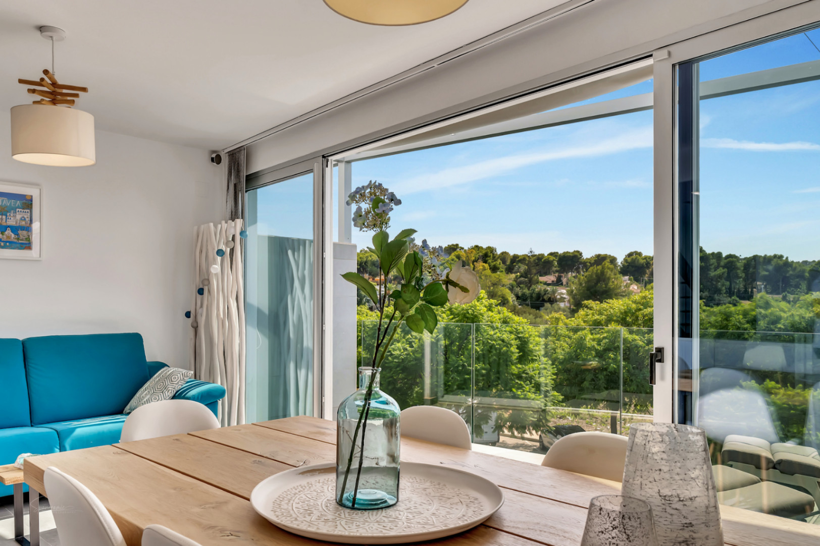 Salle à manger lumineuse avec table en bois et grandes baies vitrées coulissantes offrant une vue dégagée sur la nature environnante et un accès au balcon.