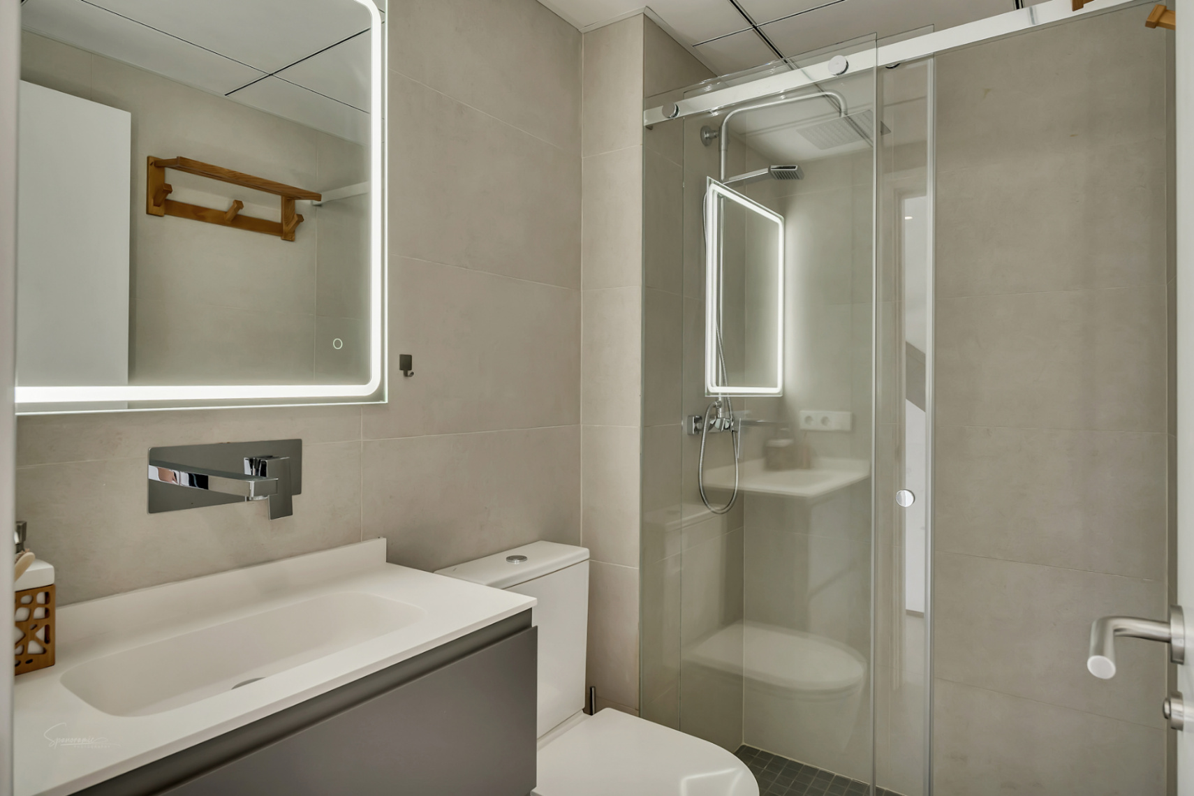 Salle de bain moderne avec carrelage neutre, miroir à éclairage LED intégré et douche à l'italienne avec paroi en verre coulissante.