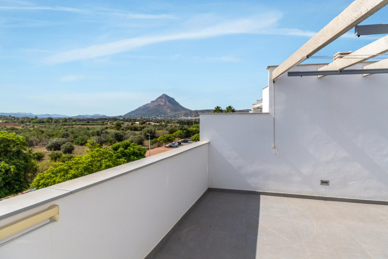 Terrasse de toit privée avec carrelage gris et pergola, offrant une vue panoramique sur la montagne Montgó et les champs verdoyants environnants.
