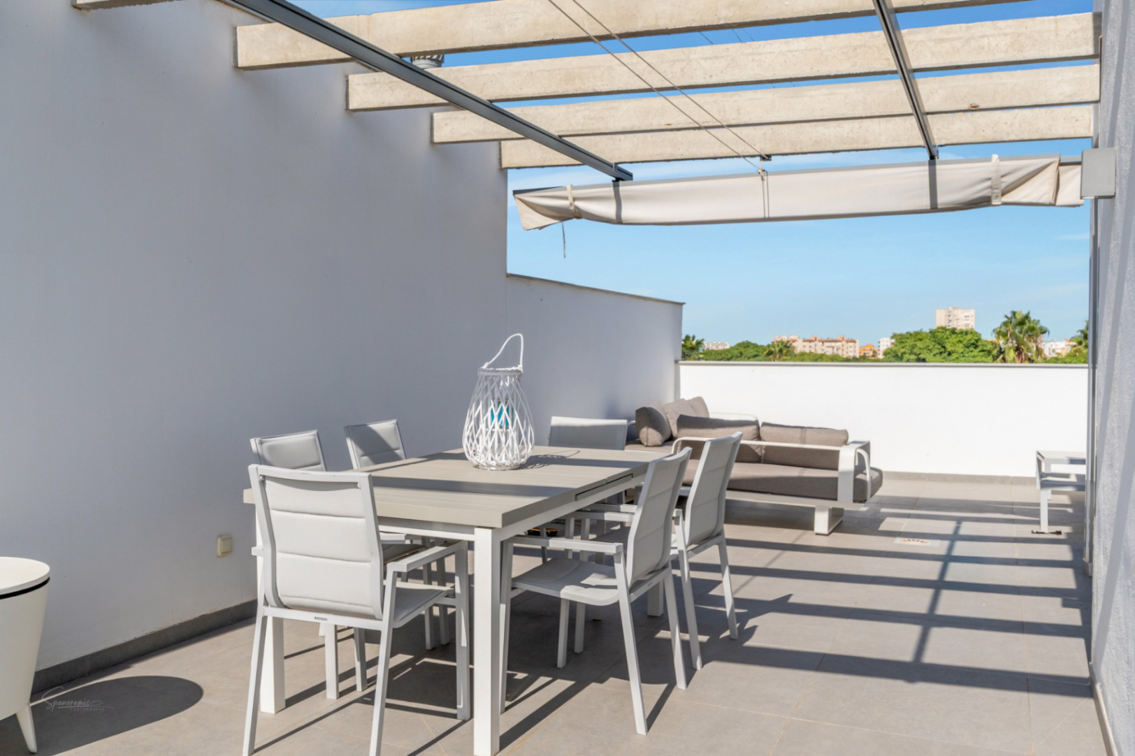 Terrasse privée sur le toit avec coin repas extérieur, canapé lounge et pergola en béton avec store rétractable sur un sol en grès gris.