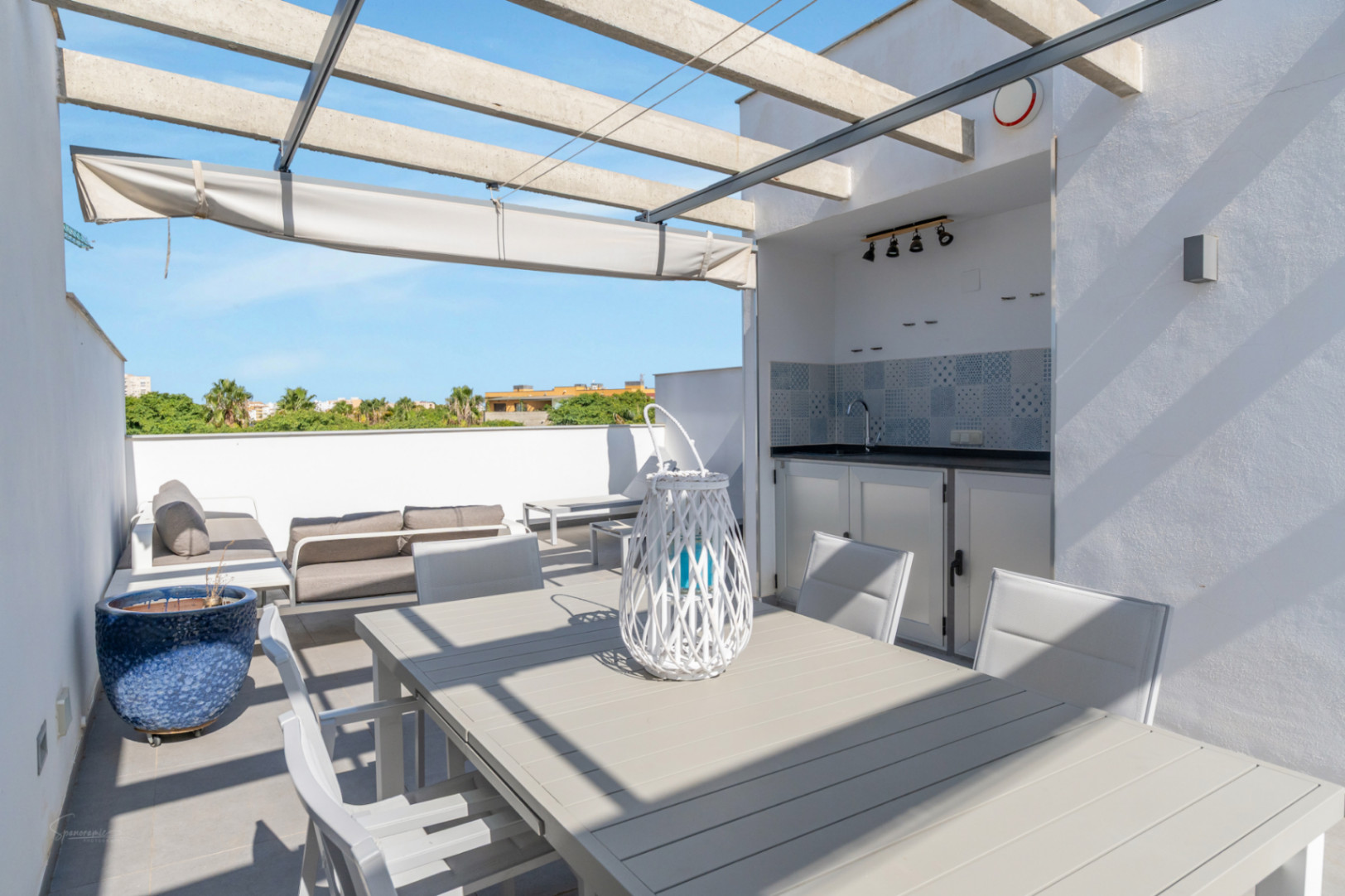 Terrasse privée sur le toit avec cuisine d'été, coin repas et salon extérieur sous une pergola en béton avec store rétractable et vue dégagée.