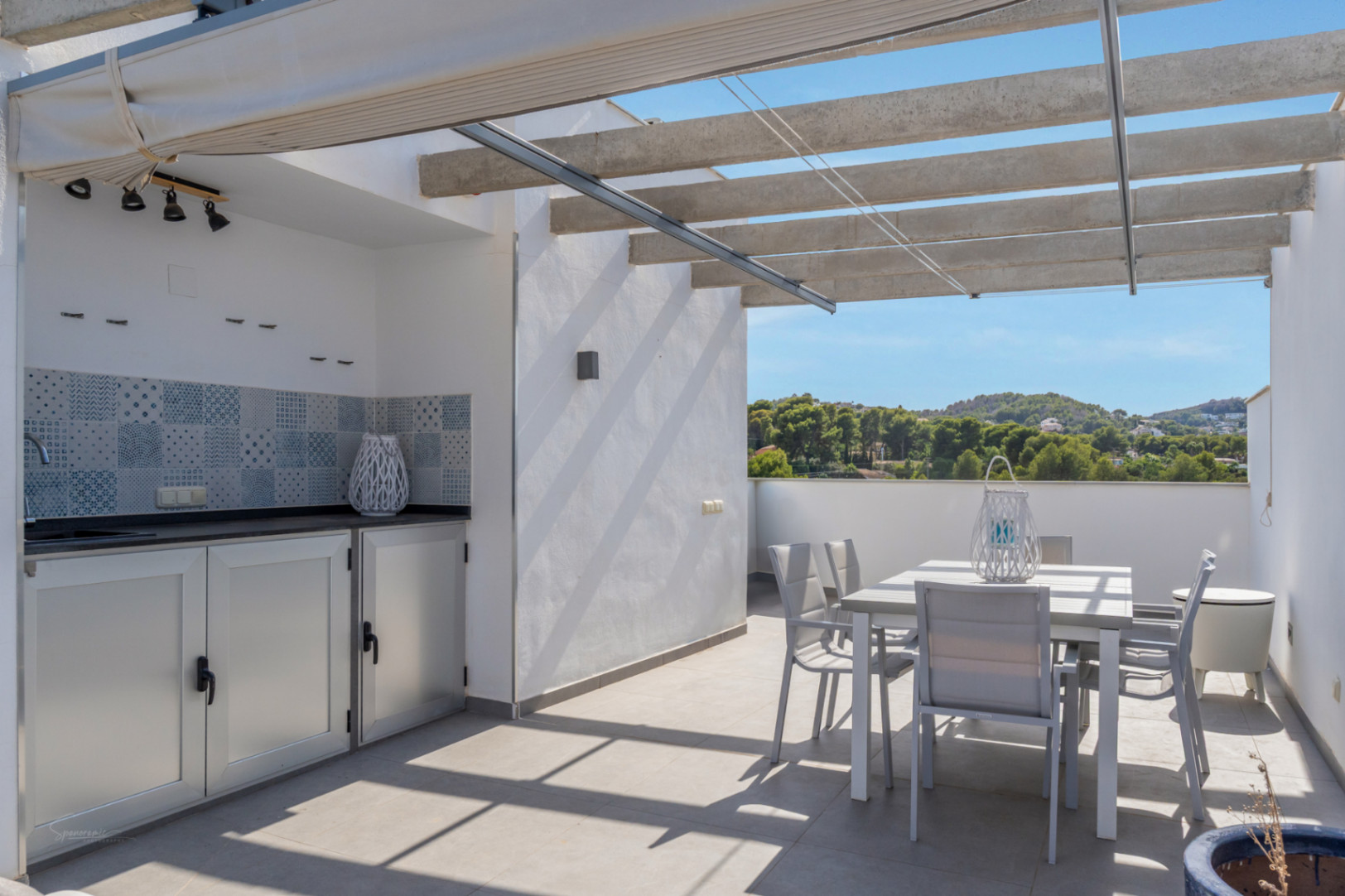 Terrasse privée sur le toit avec cuisine d'été, coin repas extérieur et pergola à auvent rétractable, offrant une vue dégagée sur les collines environnantes.