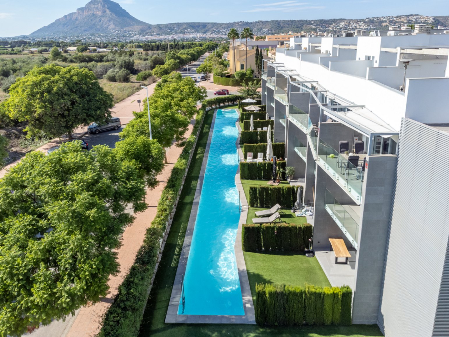 Vue aérienne de la piscine commune de 53 mètres de long, entourée de jardins privés et offrant un panorama sur les champs protégés et la montagne.