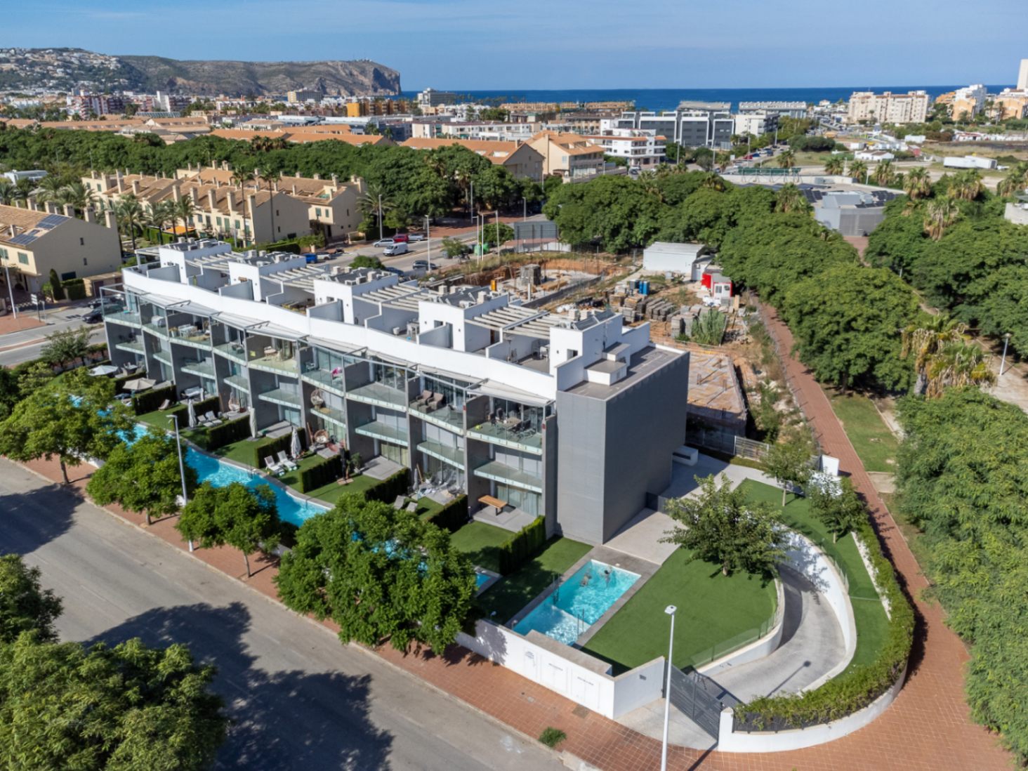 Vue aérienne du complexe résidentiel moderne avec piscines communes, jardins privés et accès au parking souterrain, situé à proximité de la mer.