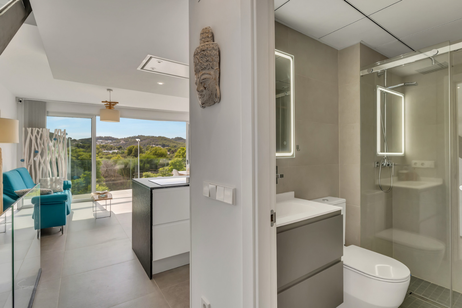 Vue du couloir montrant une salle de bain moderne avec miroir rétroéclairé et douche vitrée, ouvrant sur un salon lumineux avec accès direct à la terrasse.