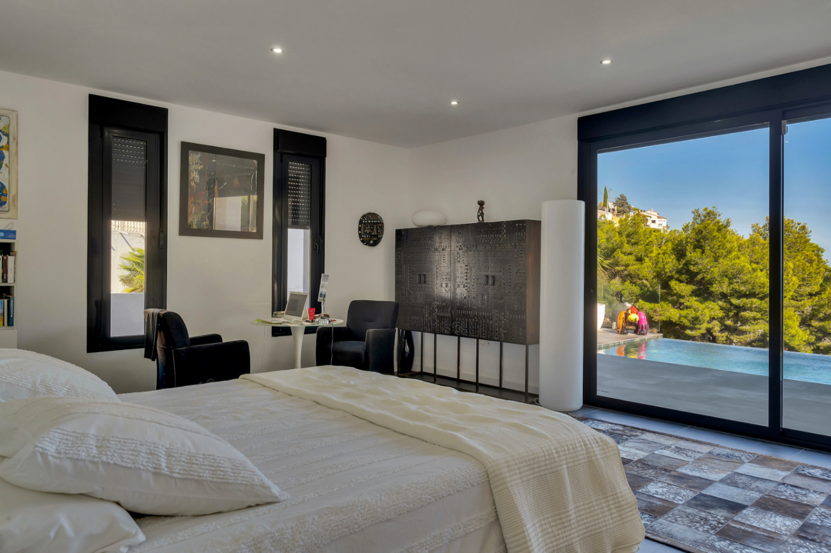 Chambre avec accès direct à la piscine, baies vitrées à cadre noir, mobilier contemporain sombre et éclairage encastré dans le plafond blanc.