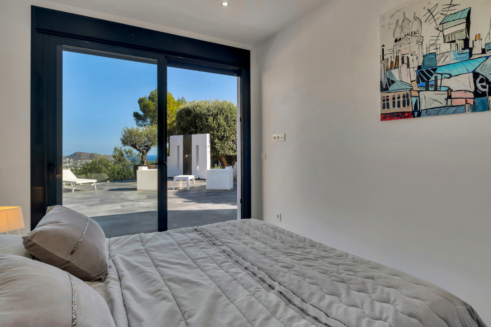 Chambre avec accès direct à la terrasse par de larges baies vitrées, offrant une vue sur la mer Méditerranée et le jardin depuis le lit.