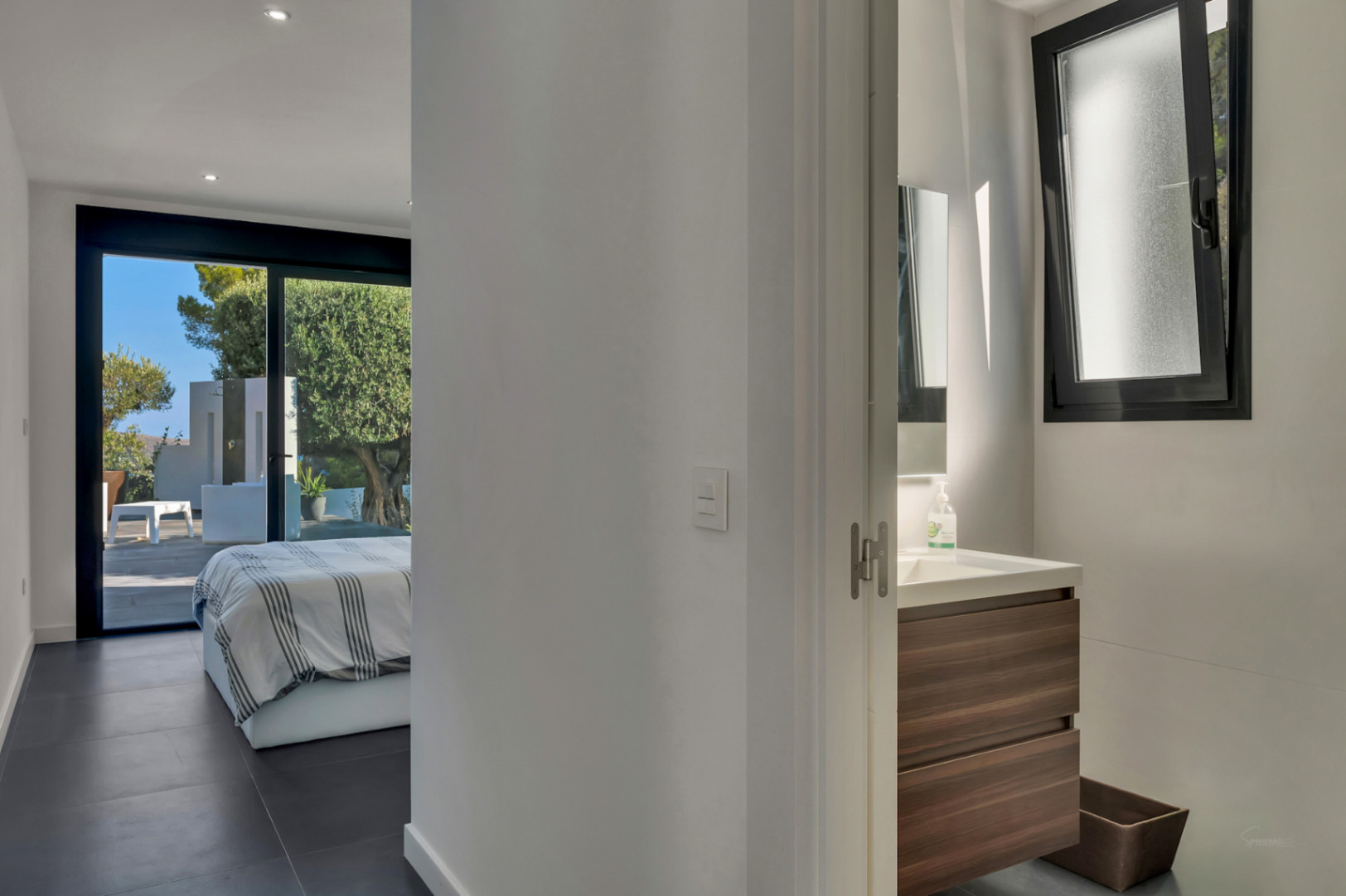 Chambre en suite avec accès direct à la terrasse, carrelage sombre et salle de bain intégrée équipée d'un meuble vasque en bois.