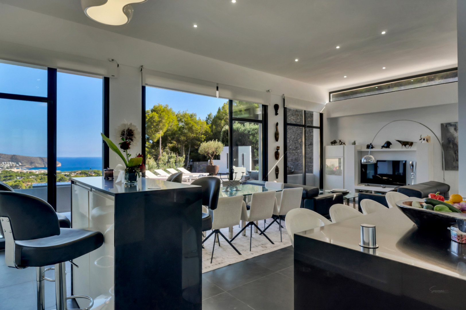 Espace de vie ouvert avec hauts plafonds, cuisine avec îlot, salle à manger et salon offrant des vues panoramiques sur la mer via de larges baies vitrées.