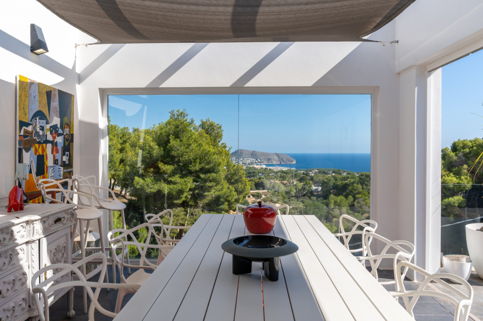 Espace repas extérieur avec table blanche et chaises design sous voile d'ombrage, offrant une vue panoramique sur la mer Méditerranée et la côte de Moraira.