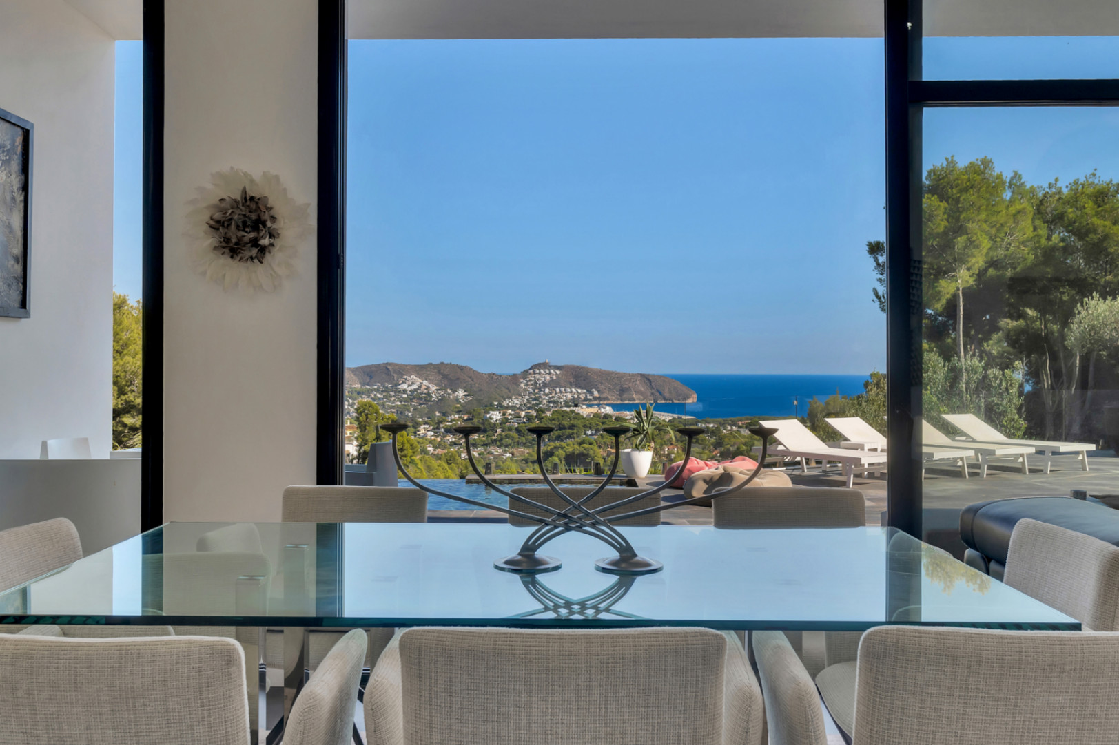 Espace salle à manger avec table en verre, offrant une vue panoramique sur la côte méditerranéenne à travers de larges baies vitrées coulissantes.