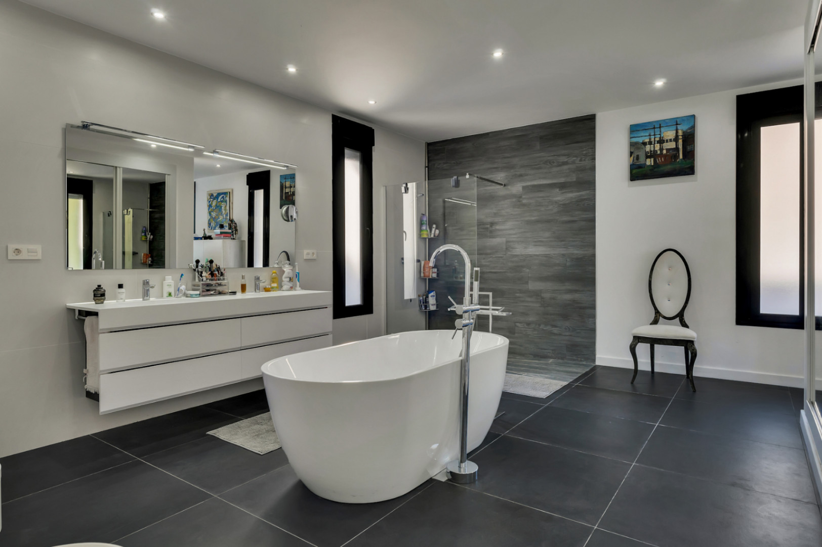 Salle de bains principale avec baignoire îlot, double vasque suspendue et douche à l'italienne avec mur en grès cérame effet bois gris.