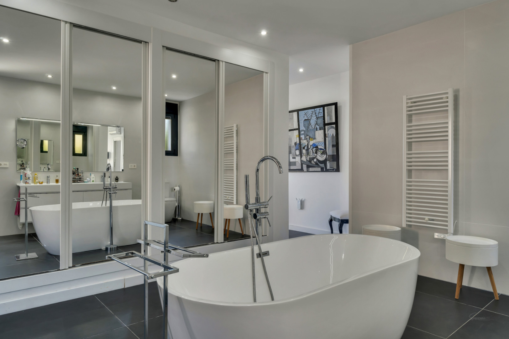 Salle de bains principale avec baignoire îlot, robinetterie sur pied chromée et grands miroirs toute hauteur accentuant le volume et la clarté.