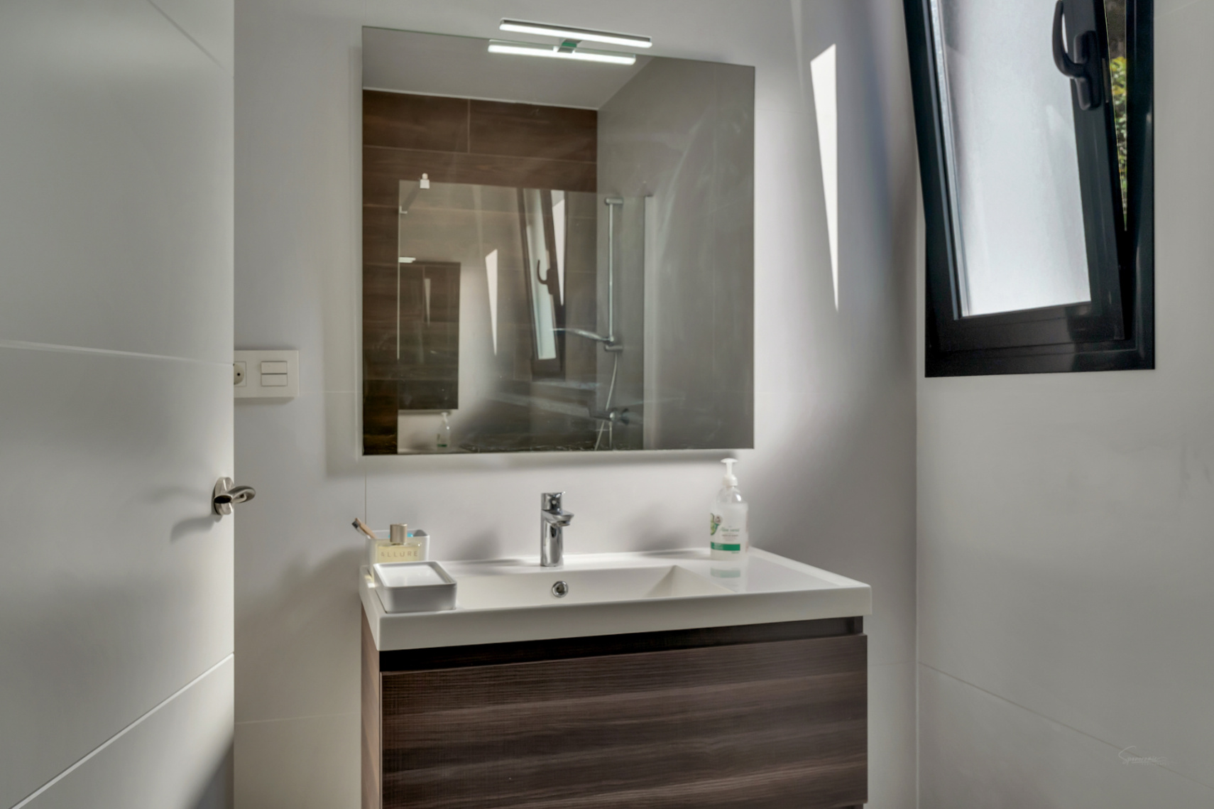 Salle d'eau contemporaine avec meuble suspendu en bois foncé, vasque blanche et miroir avec éclairage intégré. Fenêtre à cadre noir pour la lumière naturelle.
