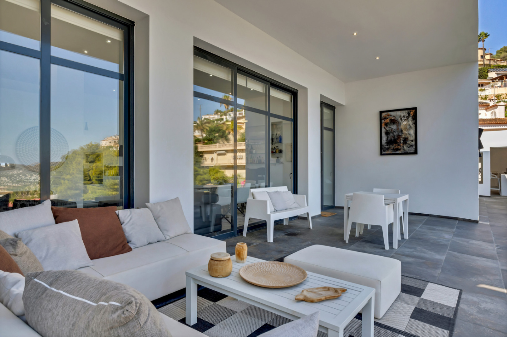 Terrasse couverte avec salon de jardin contemporain, carrelage gris et grandes baies vitrées reflétant les collines environnantes.