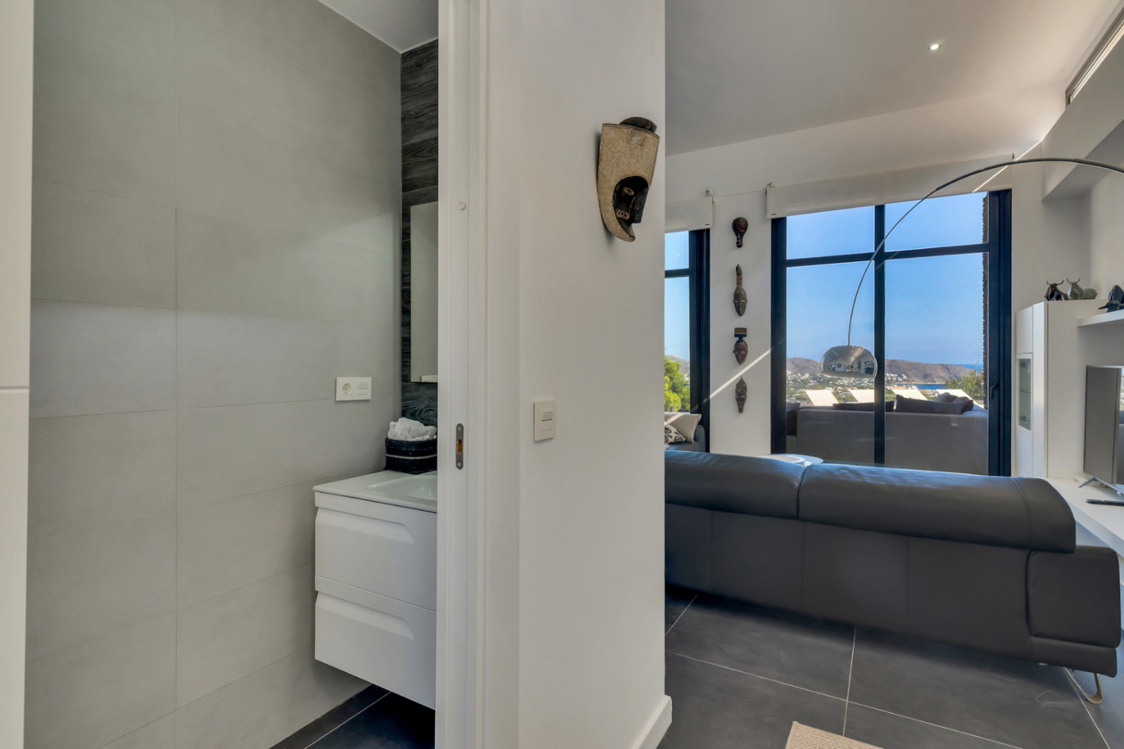 Toilettes invités avec meuble vasque suspendu, situées à côté du salon lumineux offrant une vue dégagée sur la mer et une décoration moderne.