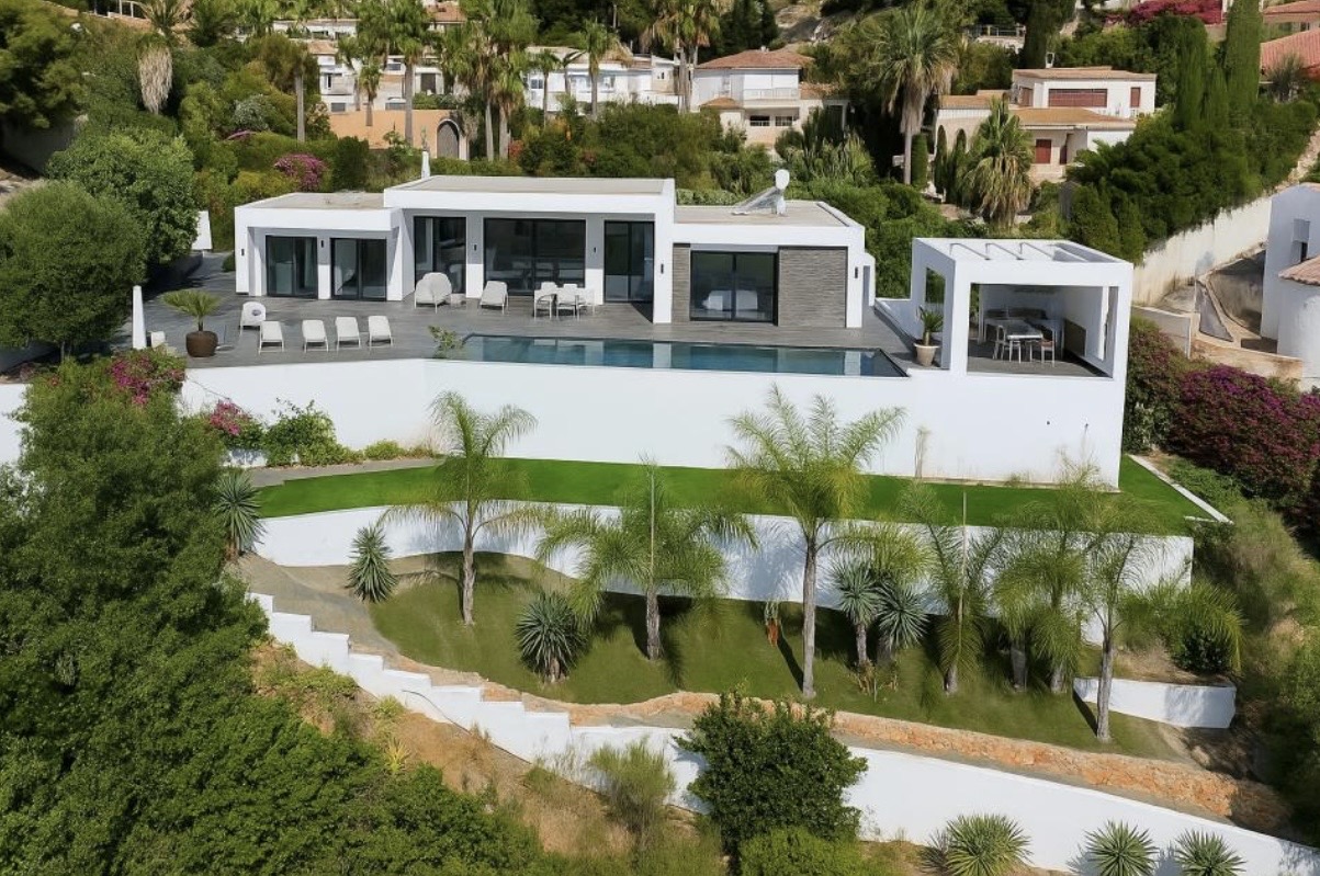 Vue extérieure de la villa moderne avec sa terrasse spacieuse, piscine à débordement et jardin méditerranéen en terrasses avec palmiers.