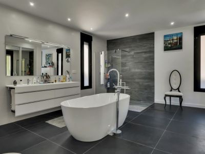 Salle de bain lumineuse avec baignoire îlot blanche, meuble-lavabo suspendu avec miroir et carrelage gris.