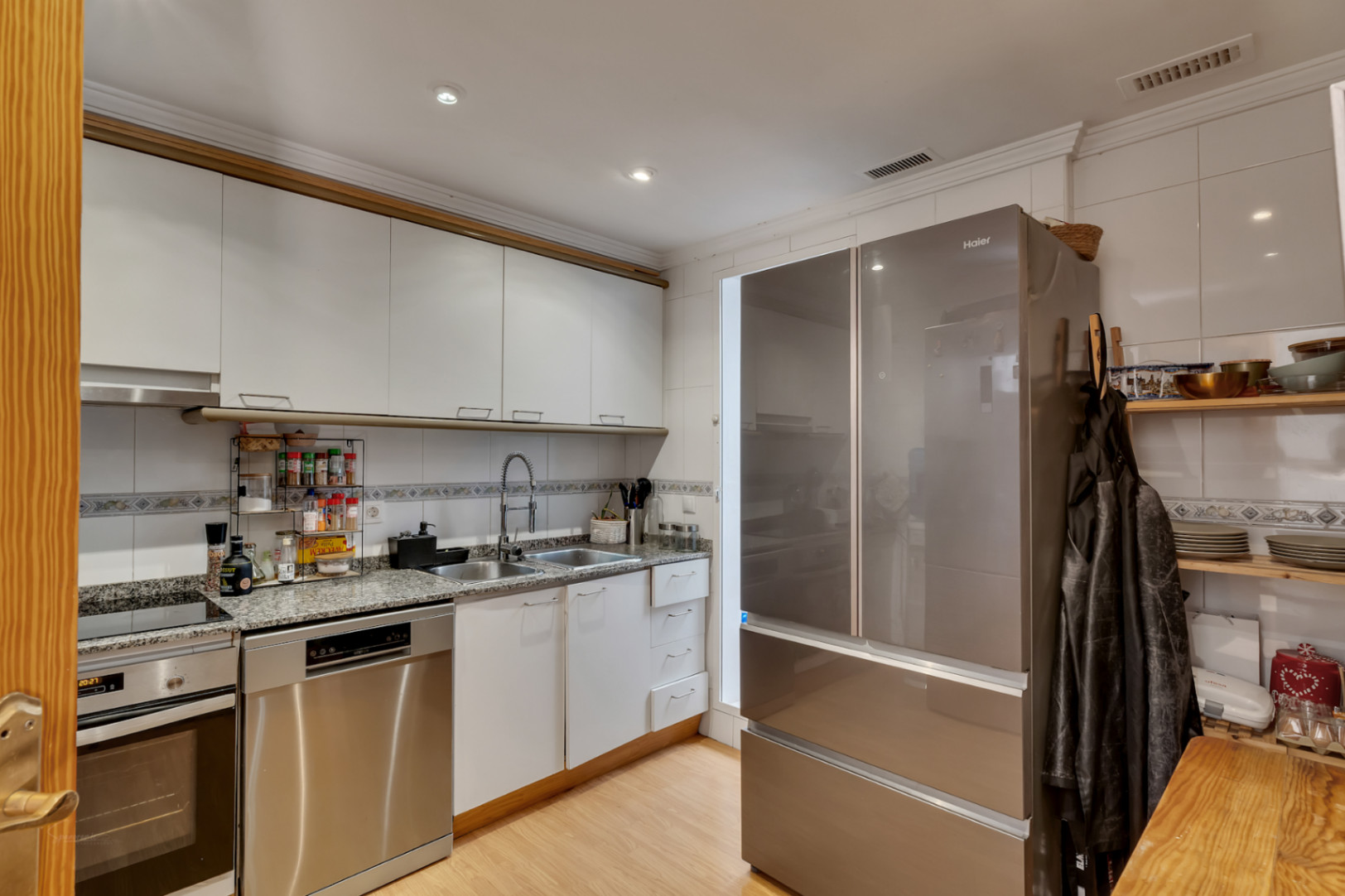 Cuisine fonctionnelle avec placards blancs, plan de travail en granit et appareils en acier inoxydable, dont un grand réfrigérateur multi-portes et un lave-vaisselle.