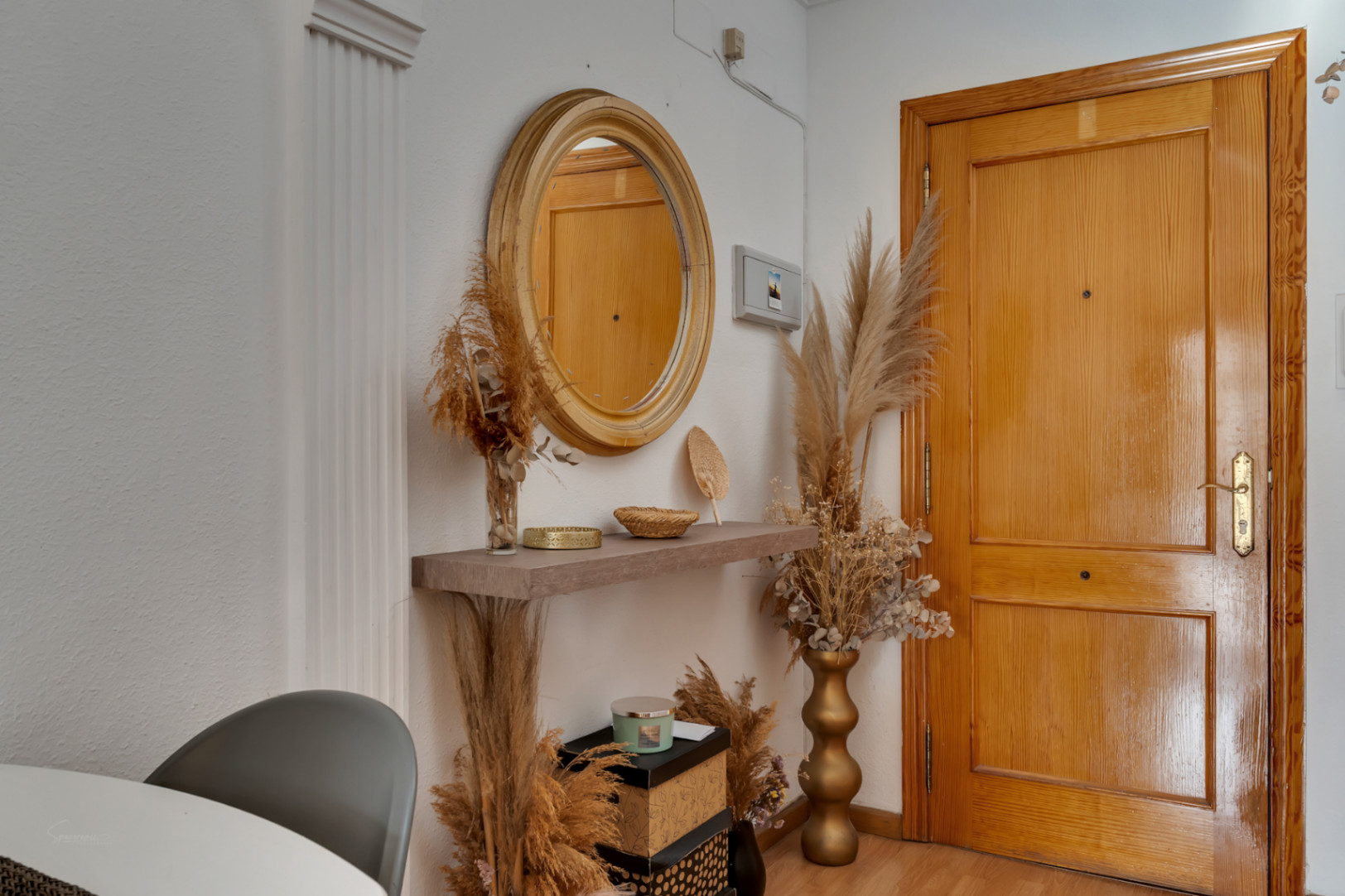 Entrée avec porte en bois massif, miroir circulaire et étagère flottante agrémentée de plantes séchées et de textures naturelles.