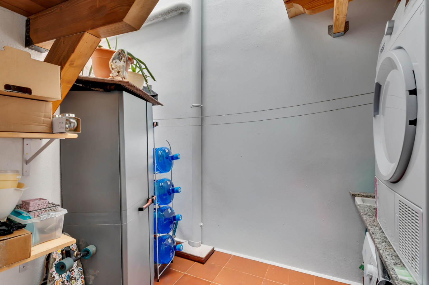 Patio intérieur fonctionnel avec espace buanderie, équipé d'un sèche-linge, d'un plan de travail en granit, d'étagères en bois et d'un sol en terre cuite.