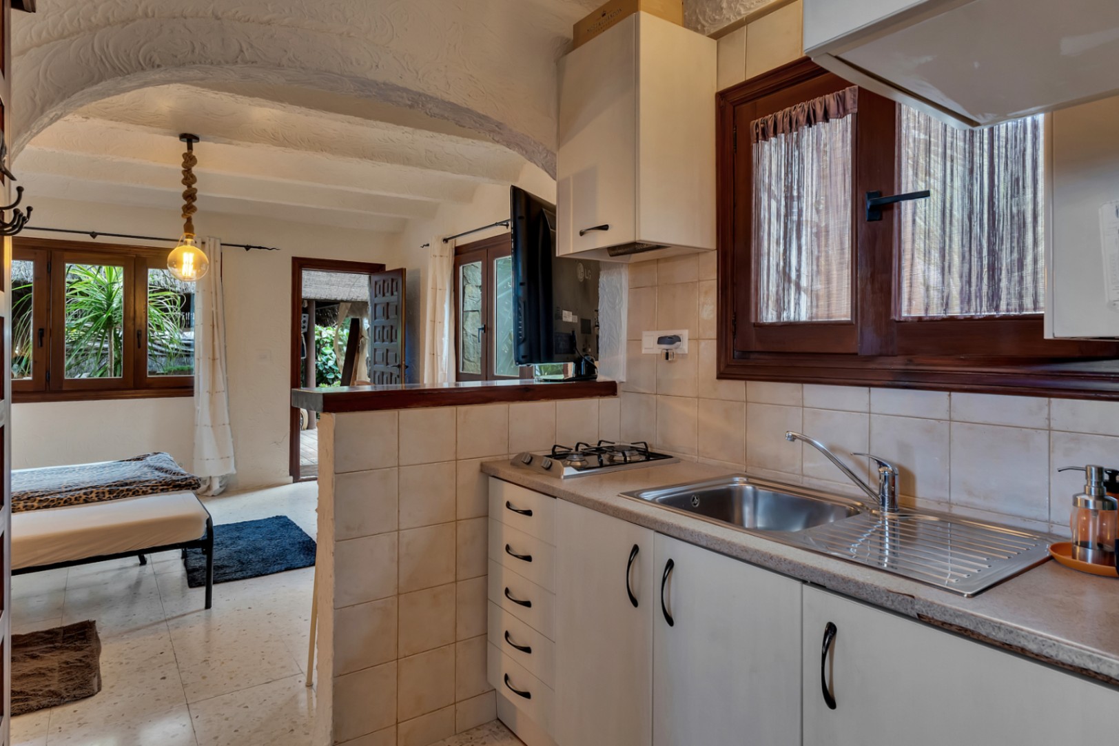 Cuisine compacte de l'appartement d'invités avec des éléments blancs, une plaque de cuisson au gaz et un plafond voûté texturé typiquement méditerranéen.