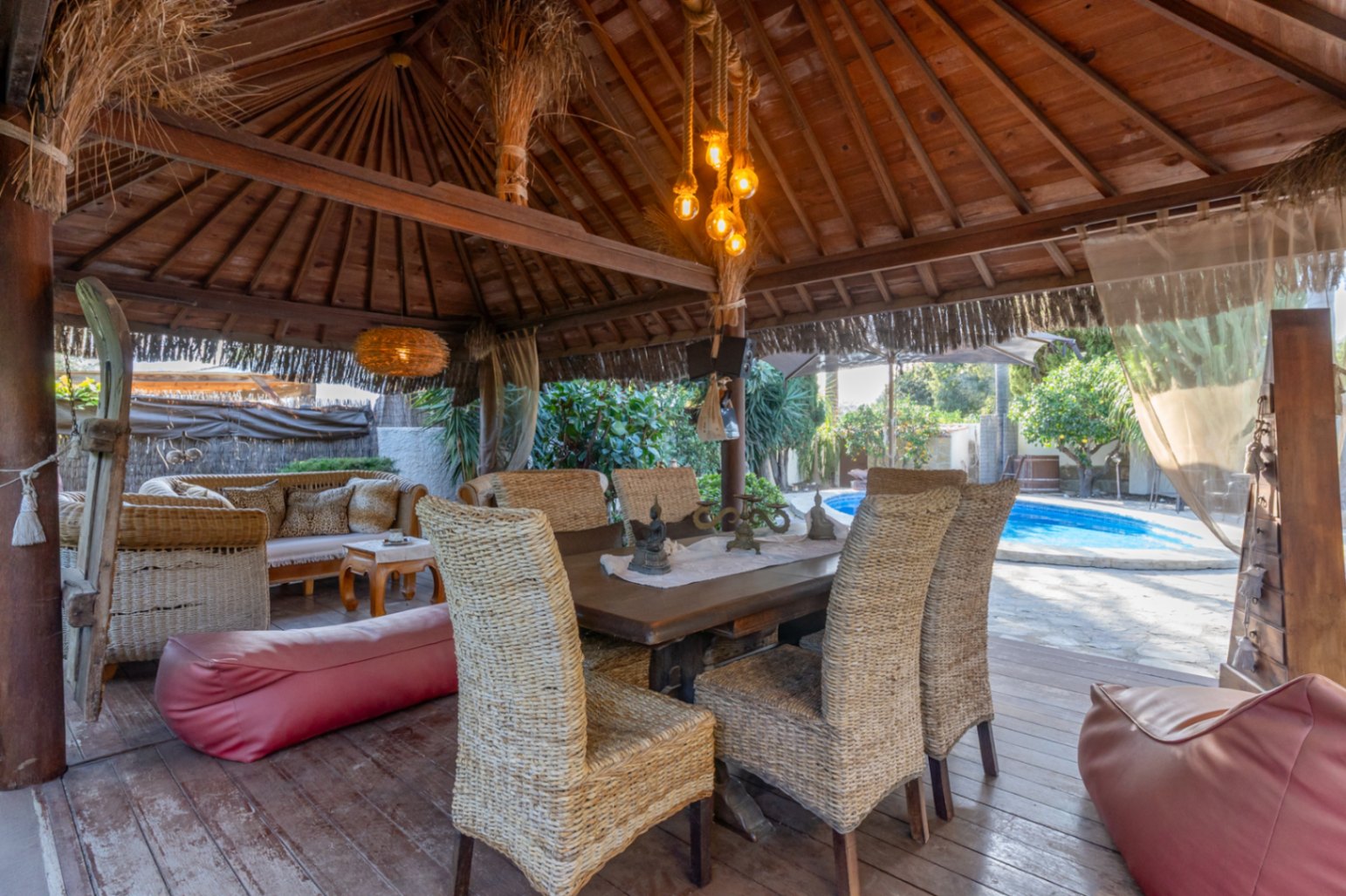Pergola en bois de style balinais avec terrasse en bois, mobilier en osier et vue directe sur la piscine privée.
