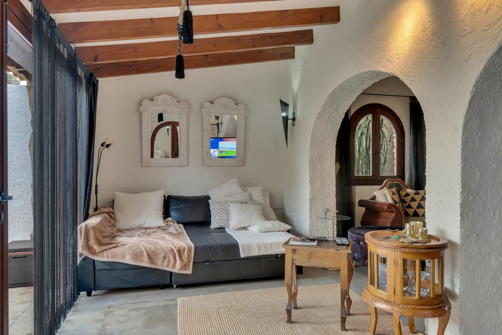 Salon chaleureux avec poutres en bois apparentes, murs à la texture rustique et arches méditerranéennes. Décoré avec un canapé en cuir et des meubles d'appoint en bois.
