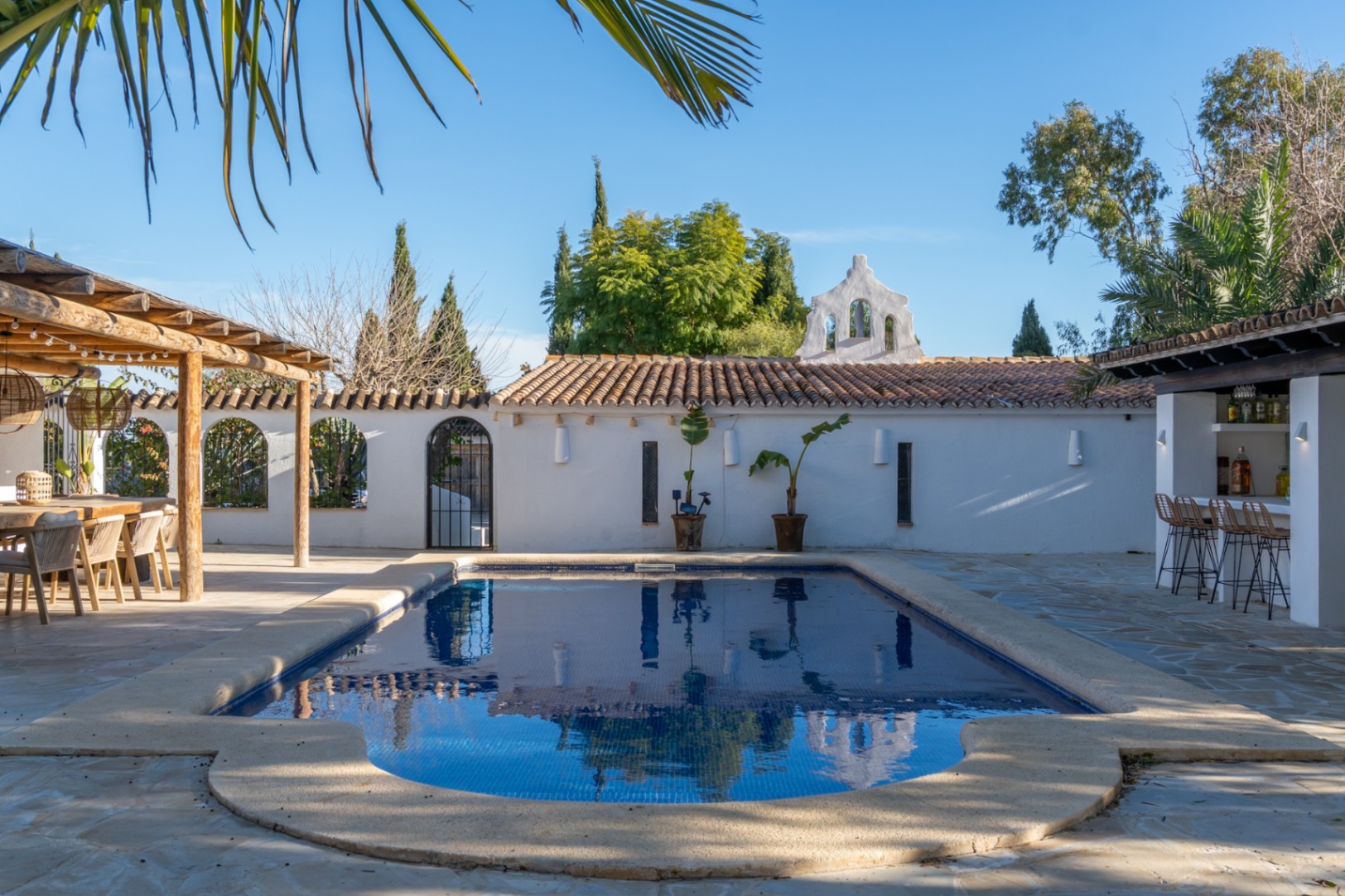 Espace piscine avec terrasse en pierre naturelle, pergola en bois pour les repas et bar d'été, le tout souligné par une architecture méditerranéenne.