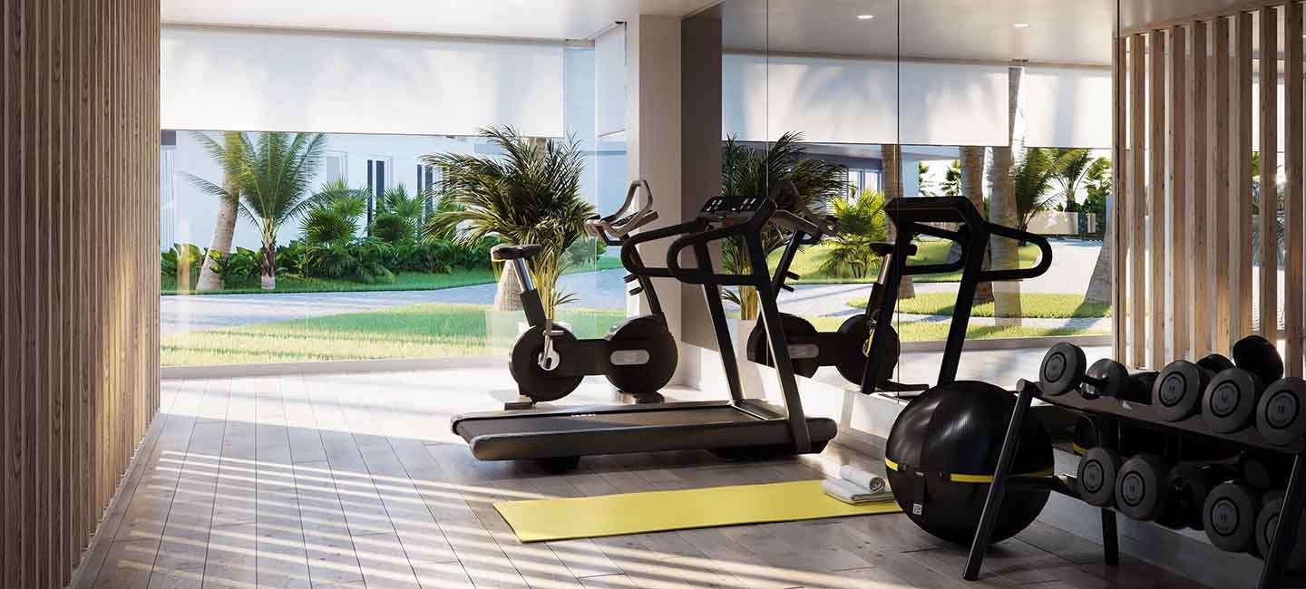 Salle de sport moderne avec équipements de cardio, poids libres et baies vitrées offrant une vue sur les jardins méditerranéens et les palmiers.