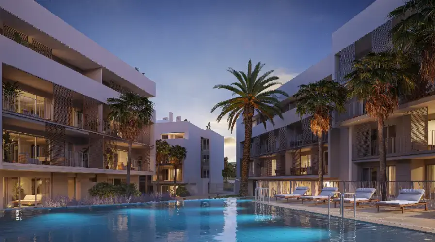 Vue extérieure de la piscine communautaire au crépuscule, avec éclairage subaquatique, chaises longues et façades blanches modernes avec brise-soleil.