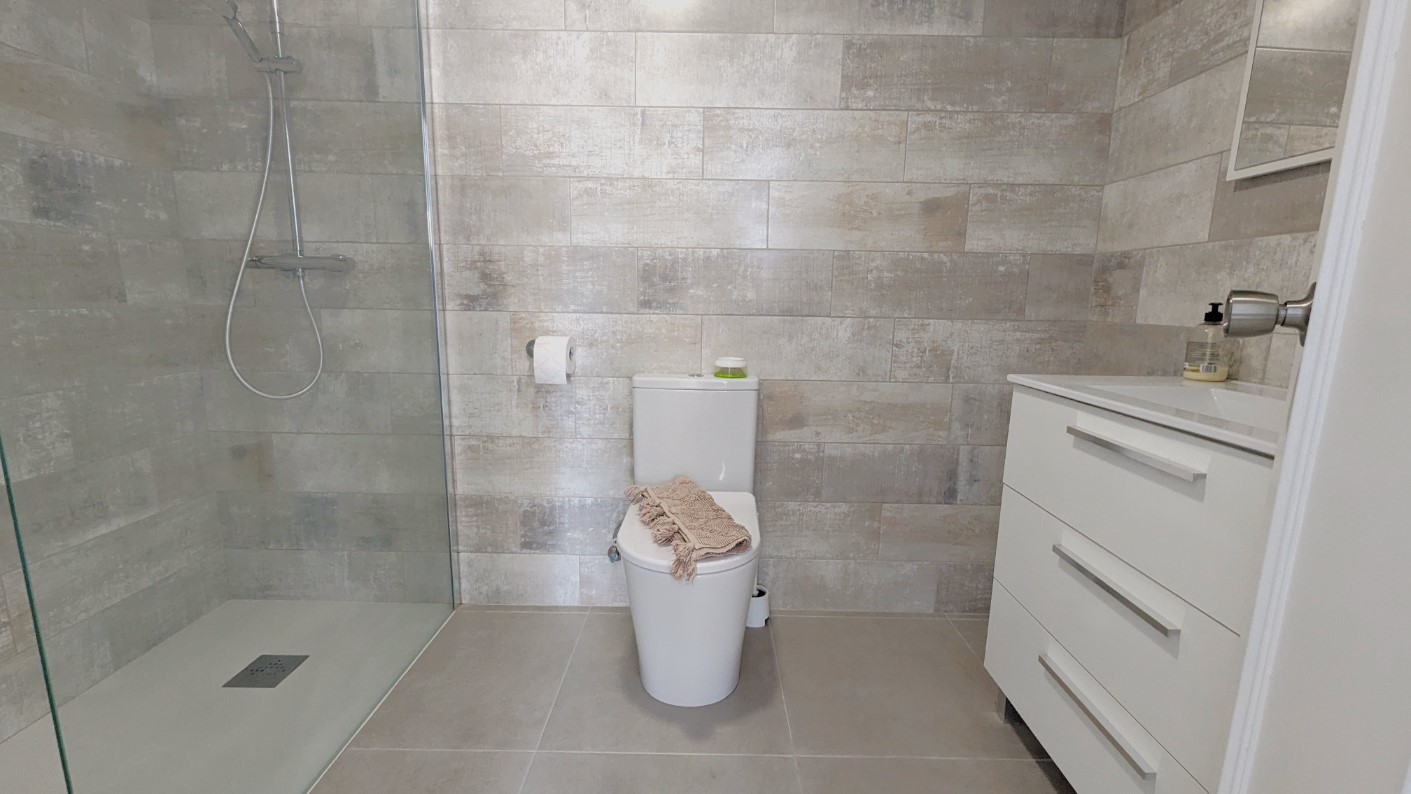 Salle de bain moderne avec douche à l'italienne, paroi en verre, carrelage mural texturé gris et meuble vasque blanc avec rangements.