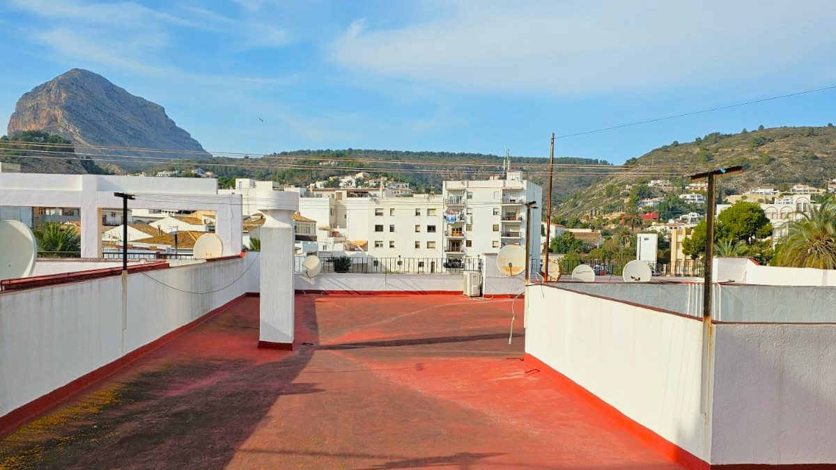 Terrasse de toit commune avec revêtement rouge, offrant une vue panoramique sur le mont Montgó et les collines environnantes de Javea.