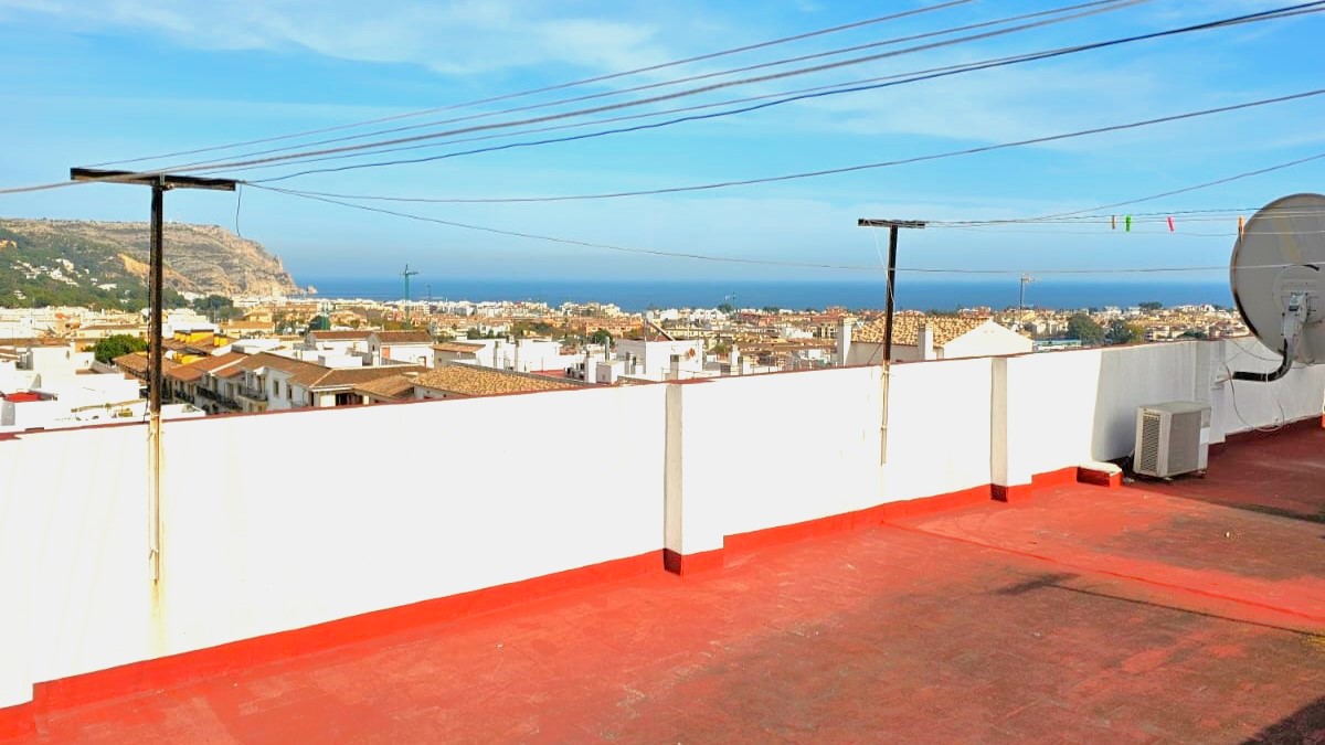 Toit-terrasse commun avec sol carrelé rouge, offrant une vue panoramique sur les toits de la vieille ville de Javea et la mer.