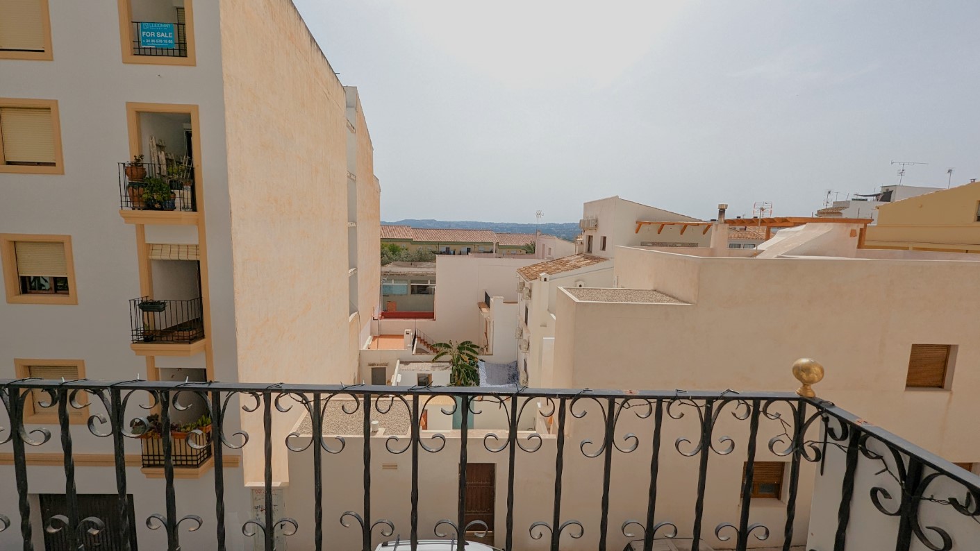 Vue depuis le balcon avec balustrade en fer forgé, donnant sur les toits de la vieille ville de Javea et les montagnes à l'horizon lointain.