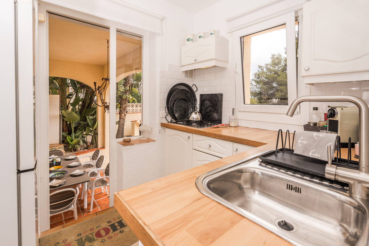 Cuisine équipée avec plans de travail en bois, carrelage métro et accès direct à une naya extérieure avec coin repas sous des arches méditerranéennes.