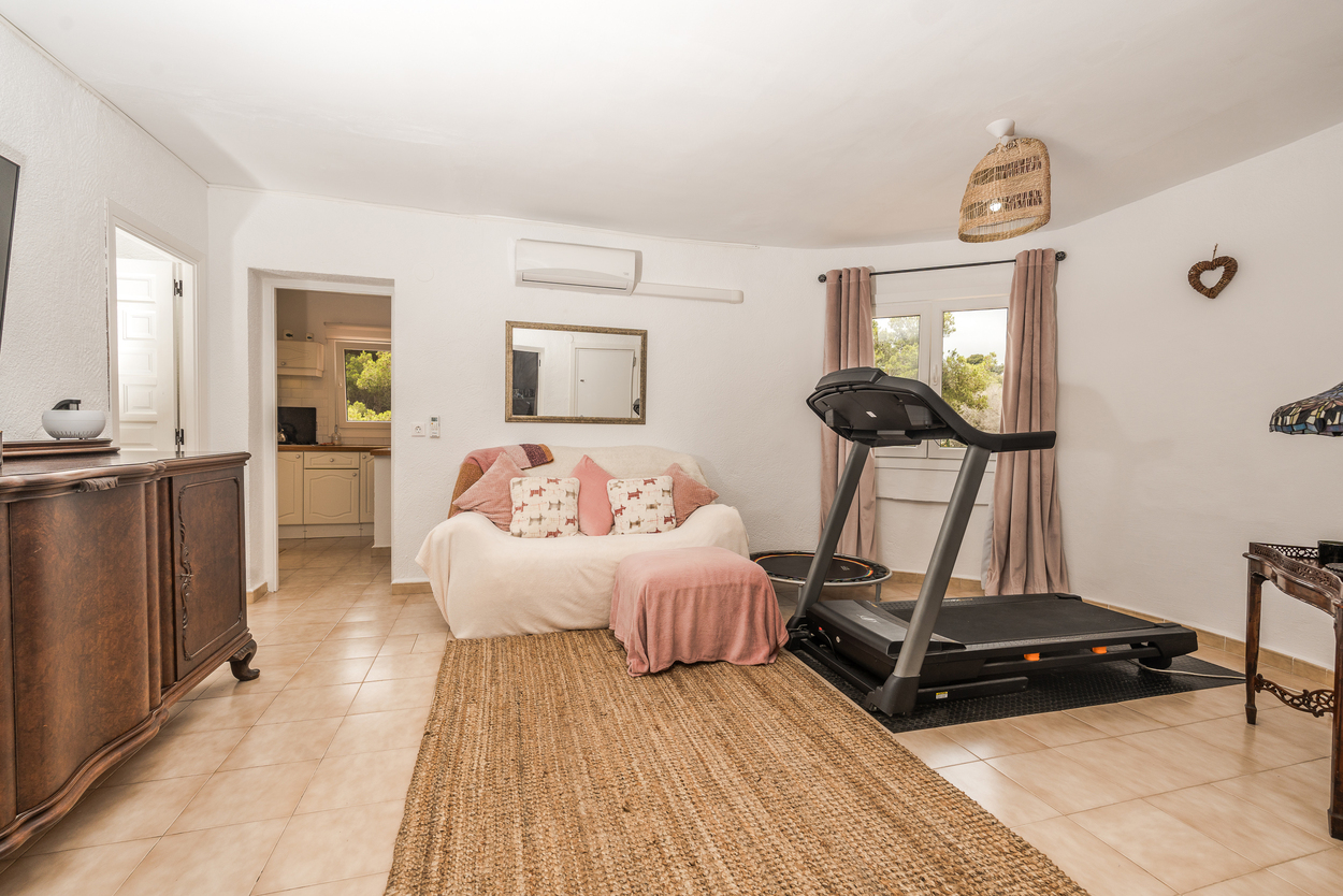 Espace de vie polyvalent avec coin fitness, tapis de course, sol en grès et climatisation, offrant une vue dégagée vers la cuisine.